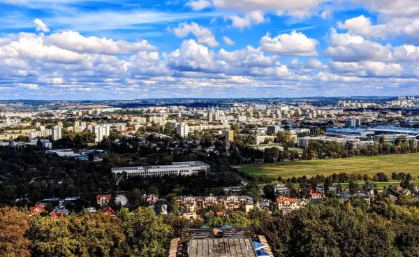 Widok na rozległe osiedla Krakowa, gdzie ceny mieszkań mogą być wysokie. W oddali widać zabudowania i zieleń.