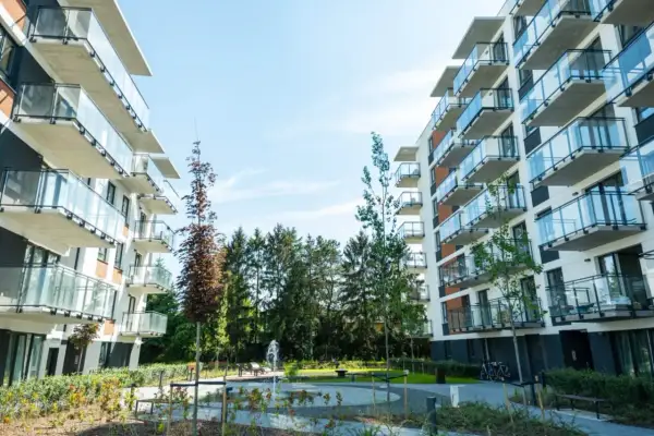 Nowoczesne apartamentowce z balkonami i szklanymi balustradami, otoczone zielenią. Idealne miejsce na inwestowanie w nieruchomości.