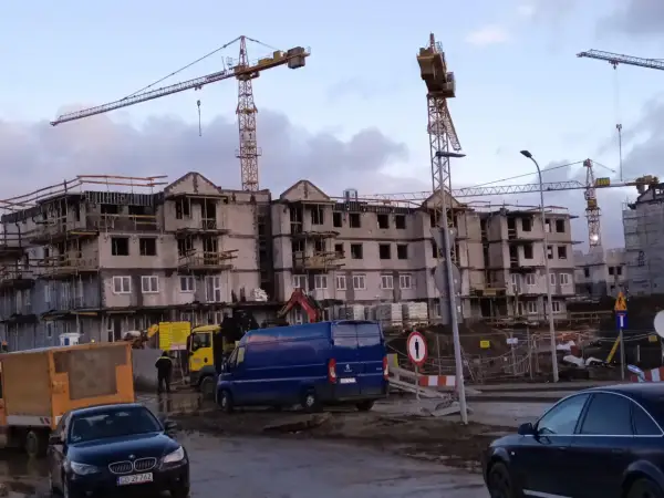 Budowa bloków mieszkalnych w Gdańsku. W tle dźwigi budowlane, na pierwszym planie samochody i maszyny budowlane. Ceny mieszkań gdańsk mogą być wysokie.