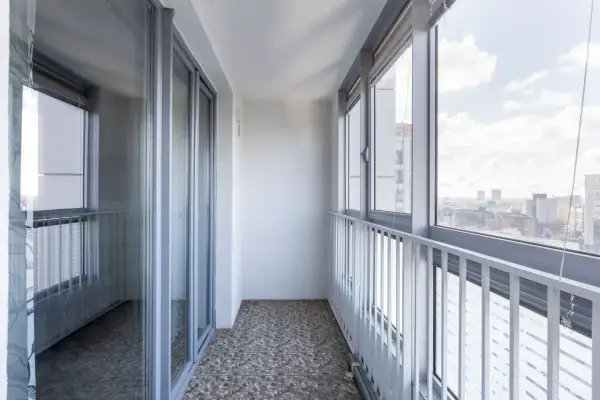 Balkon z widokiem na miasto, jak z wieży Merdeka 118. Szklane drzwi i okna, biała balustrada.