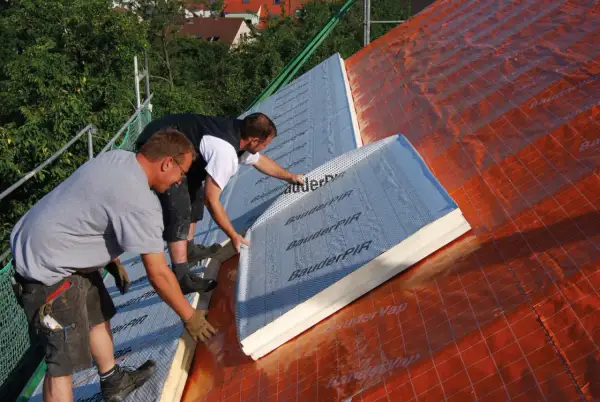 Dwaj pracownicy montują płyty izolacyjne na dachu. To kluczowy etap prac nad ociepleniem nakrokwiowym, zapewniającym komfort termiczny budynku.