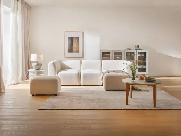 Przytulny salon z kanapą i pufą w odcieniach beżu. Beżowy kolor ścian tworzy ciepłą atmosferę.