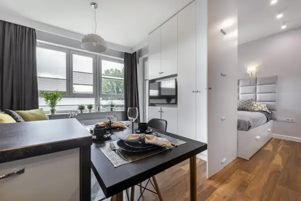 Stylowa garsoniera z aneksem kuchennym, jadalnią i wydzieloną sypialnią. Eleganckie meble i detale tworzą przytulną atmosferę.